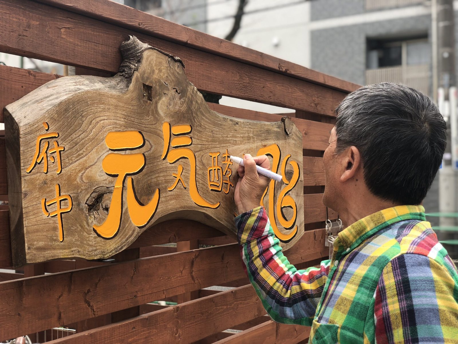 木彫りの「府中 元気酵素風呂」の看板に、創業者みずから筆を入れているところ